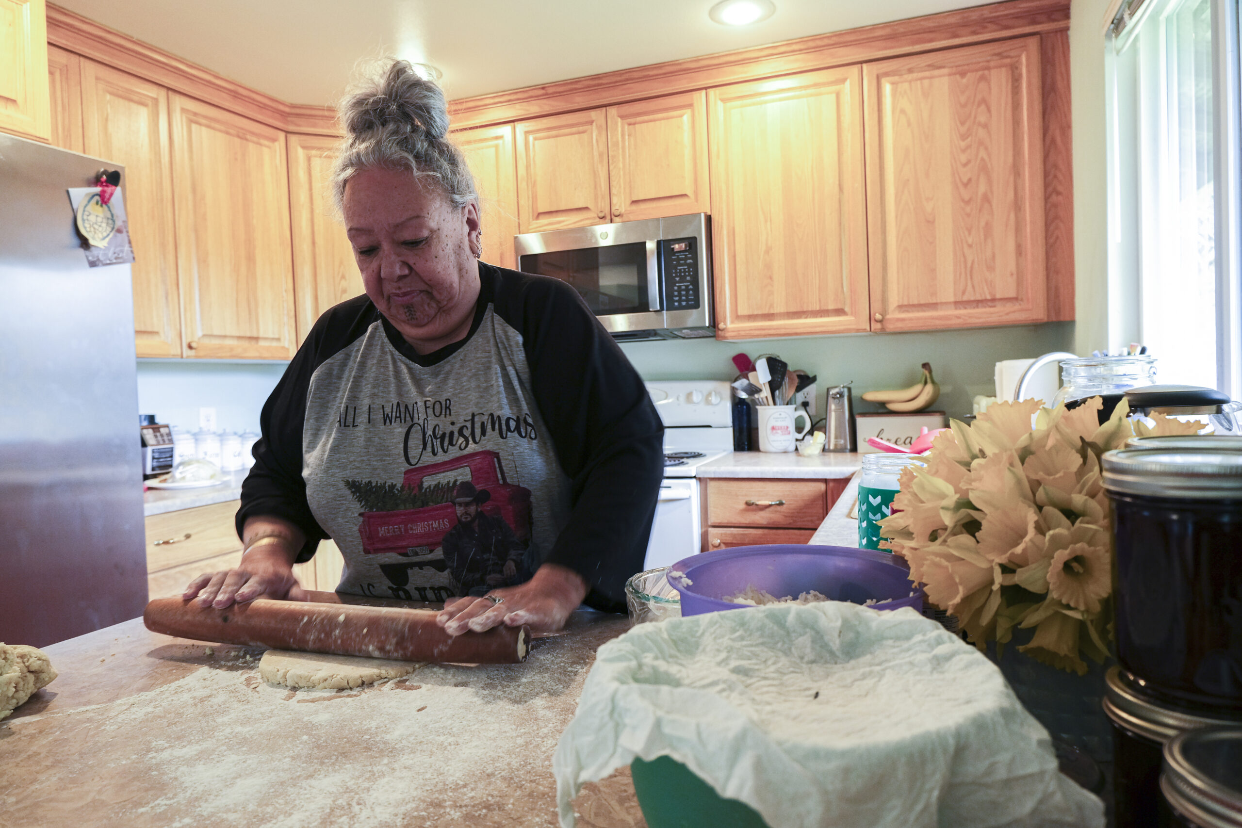 Unangax̂ woman rolling out pie dough on her kitchen counter.
